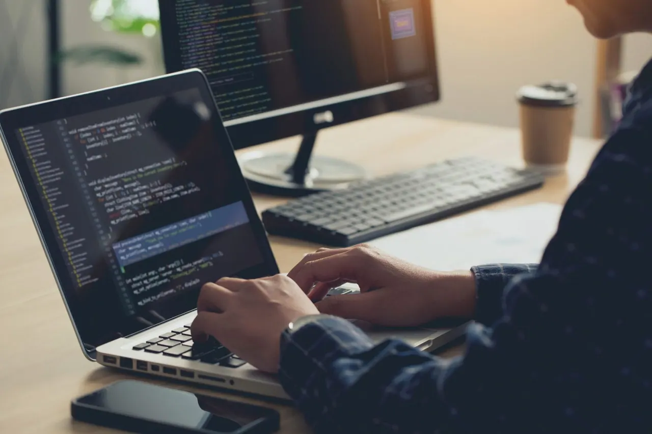 Developer writing code on a laptop beside a second monitor